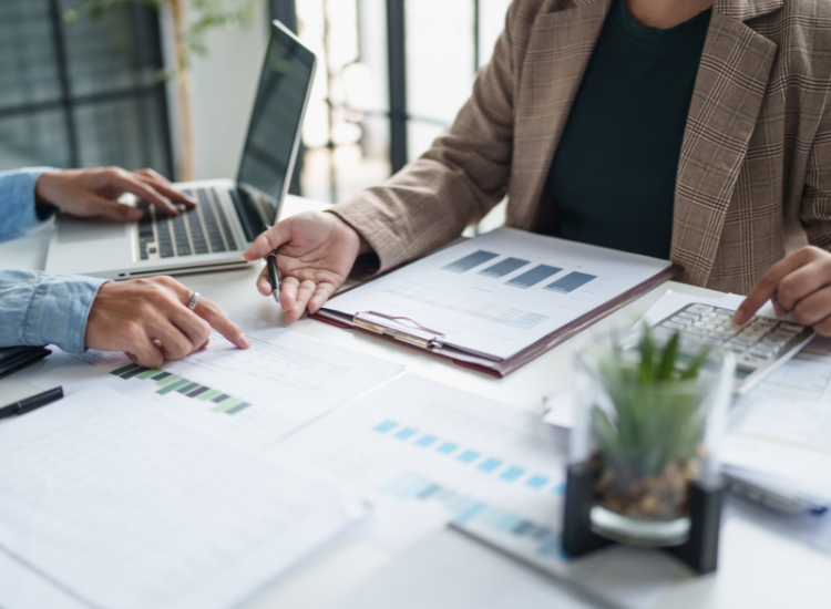 Bouclement comptable un moment clé pour la santé financière de votre PME Un homme et une femme d’affaires échangent autour d’un bureau avec des documents comptables, une calculatrice et un ordinateur, symbolisant la rigueur du bouclement comptable.