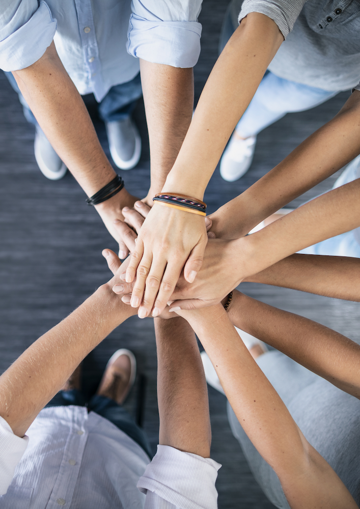 Six jeunes professionnels posent leurs mains ensemble en signe d’unité et de confiance, symbolisant la collaboration et le partenariat humain au cœur d’une fiduciaire moderne et digitale en Suisse.